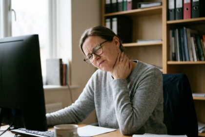 Femme souffrant de douleurs cervicales en travaillant sur ordinateur avec des lunettes mal adaptées